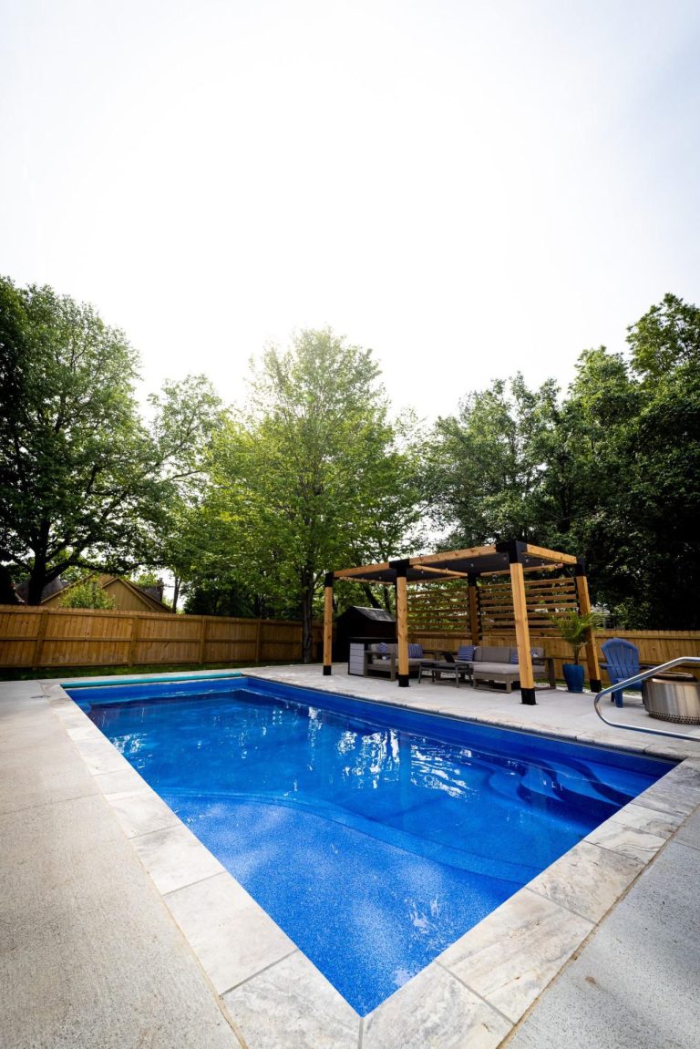 Geometric pool with seating area underneath a wooden pergola - Pools By York