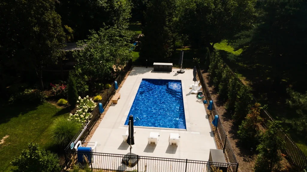 Drone view of a fenced rectangular fiberglass pool with lounge chairs