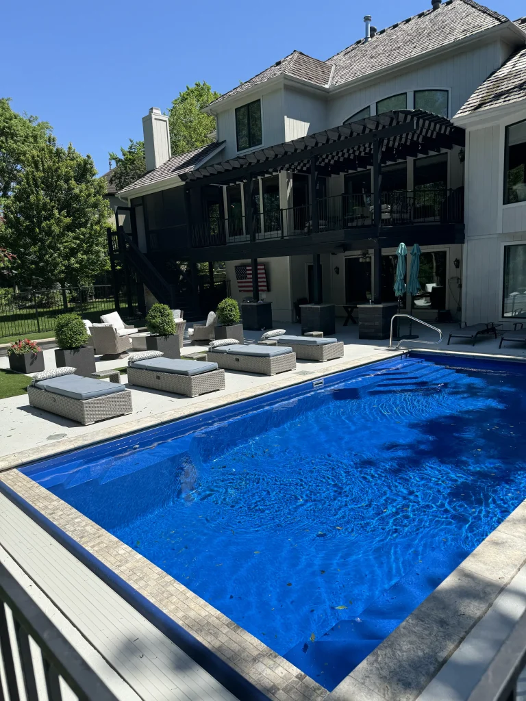 Fiberglass pool with travertine coping beside a stone patio