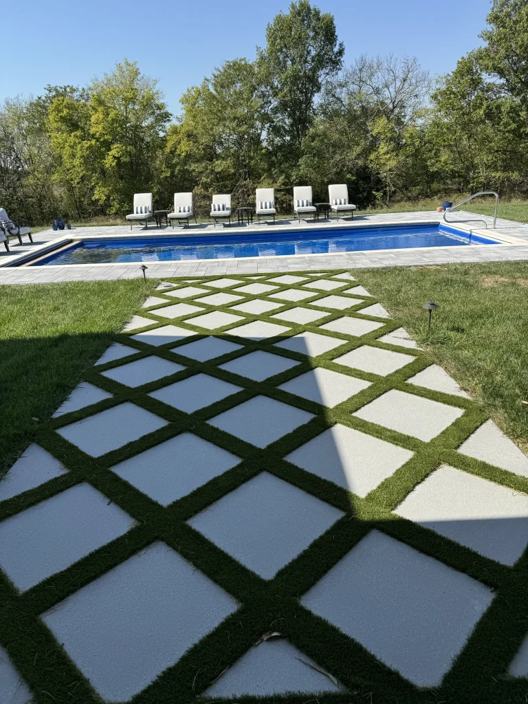 Paver and grass walkway leading to a rectangular fiberglass pool