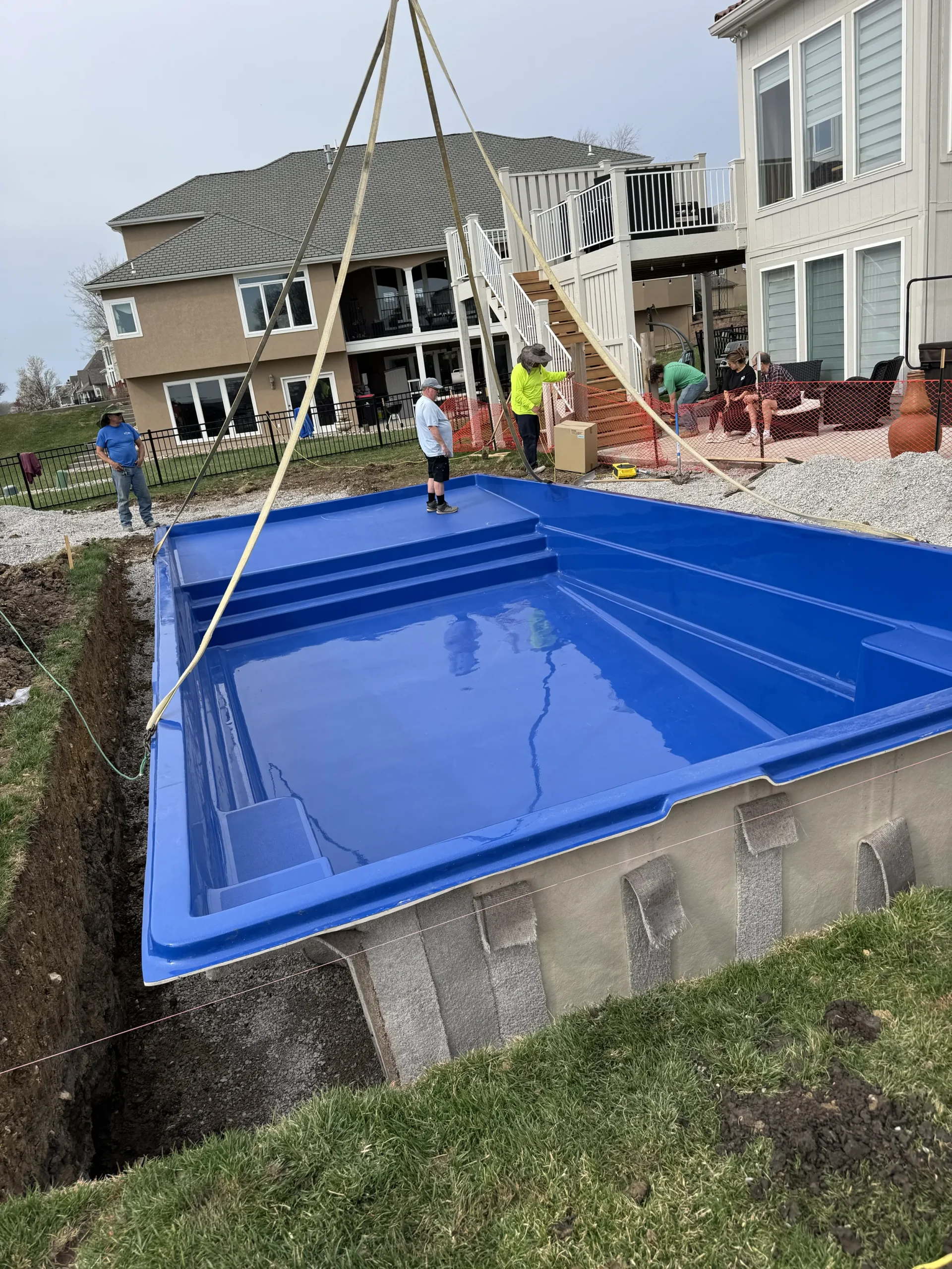 Crane lowering a fiberglass pool shell into place during installation