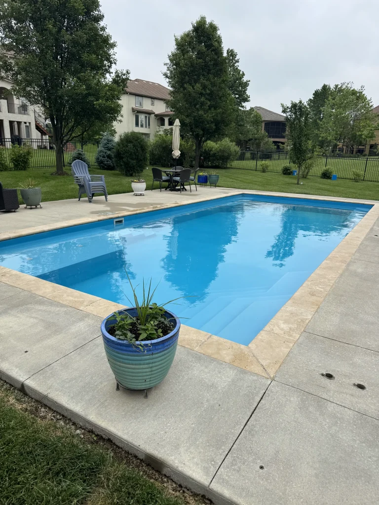 Rectangular fiberglass pool with a concrete deck and potted plant