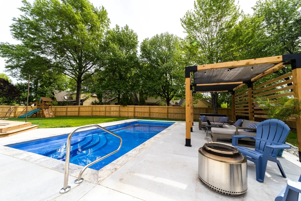 Fiberglass pool with entry steps and handrail beside a cedar pergola patio