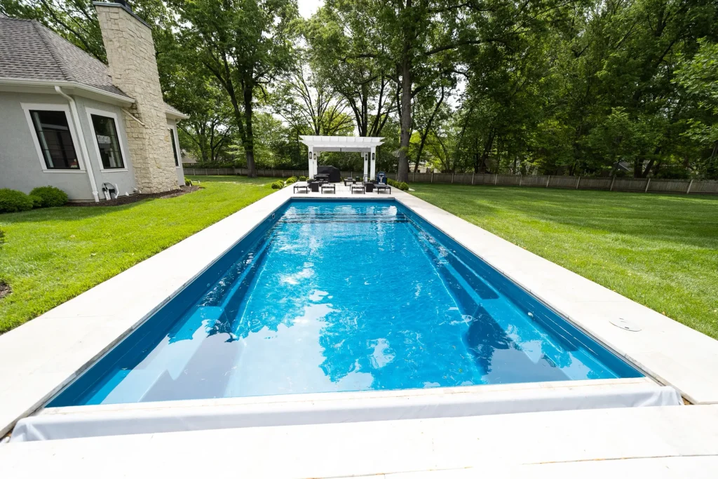 Rectangular fiberglass lap pool surrounded by lawn and a white pergola
