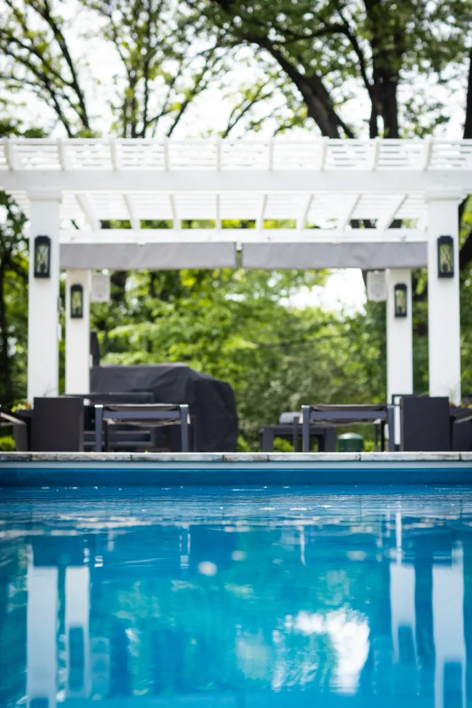 Fiberglass pool facing a white pergola with outdoor kitchen