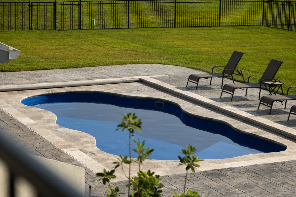 Freeform fiberglass pool with travertine coping and lounge chairs