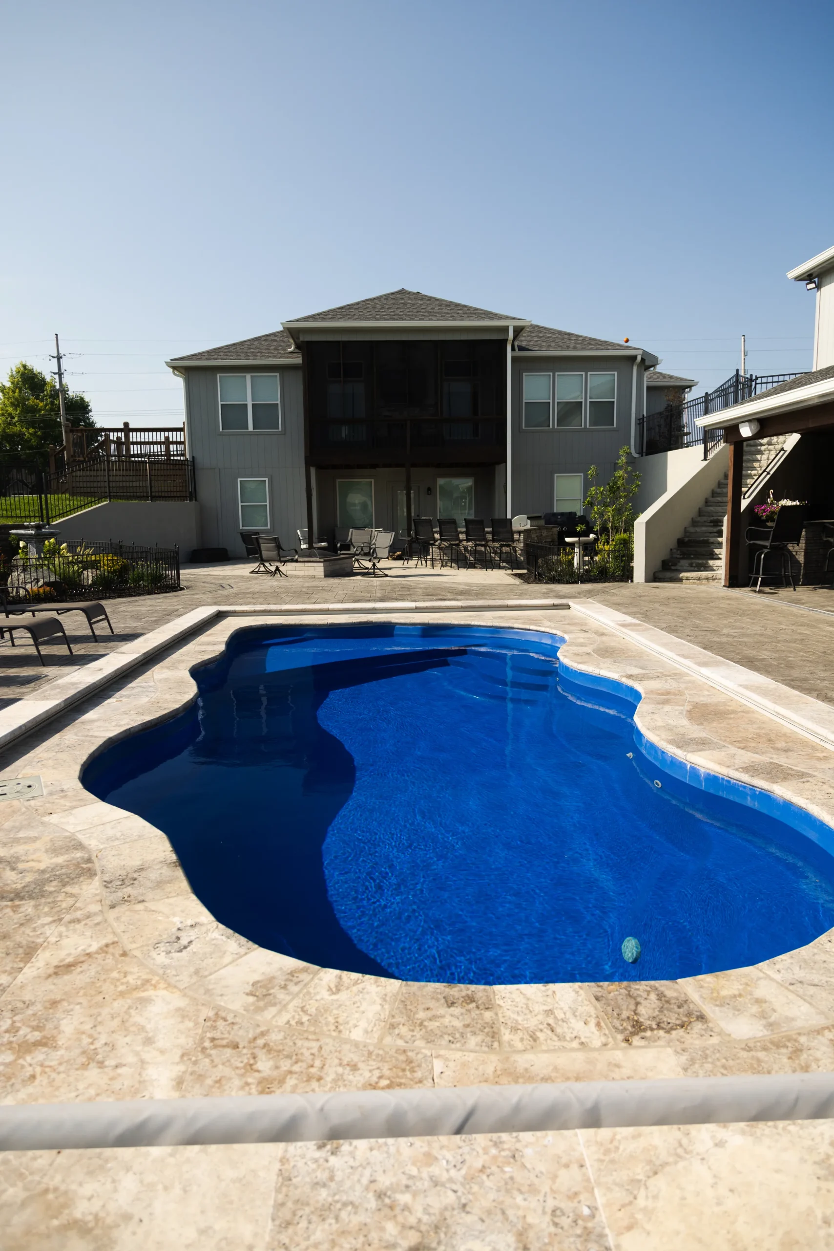 Kidney-shaped fiberglass pool with travertine deck and covered patio