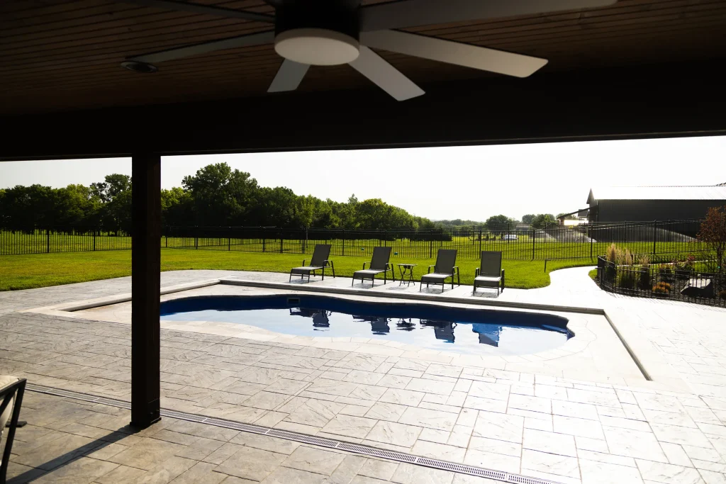 Freeform fiberglass pool viewed from a covered patio with ceiling fan