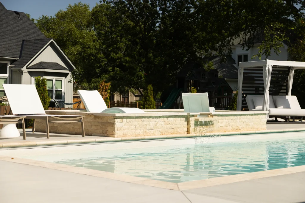 Fiberglass pool with raised stone wall and white lounge chairs
