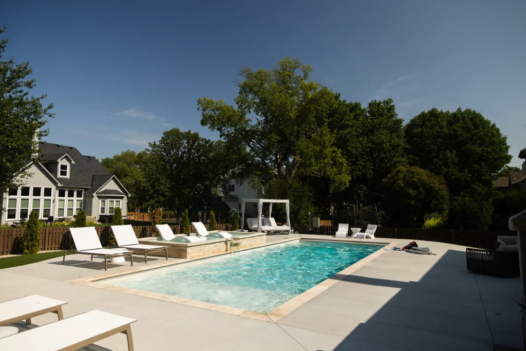 Rectangular fiberglass pool with spa and white lounge chairs