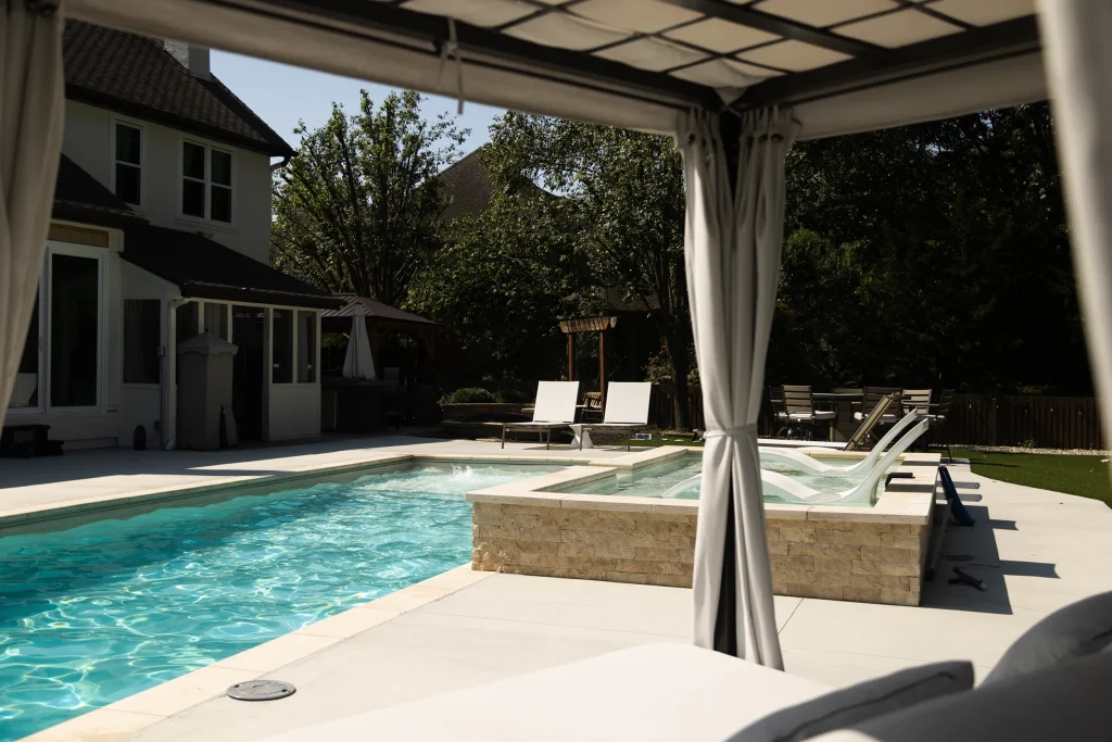 Fiberglass pool and raised spa viewed from a curtained cabana