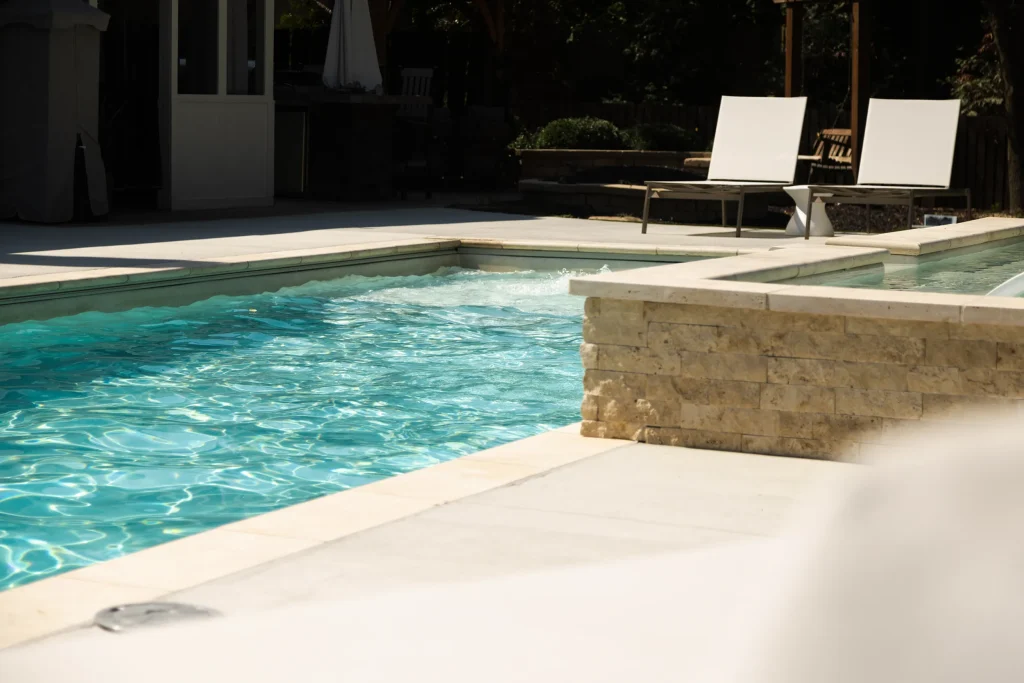 Fiberglass pool with a raised stone spa wall and lounge chairs