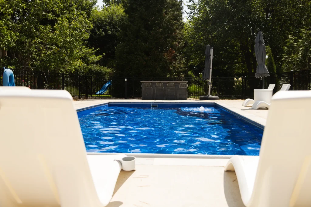 Fiberglass pool viewed between two white poolside loungers