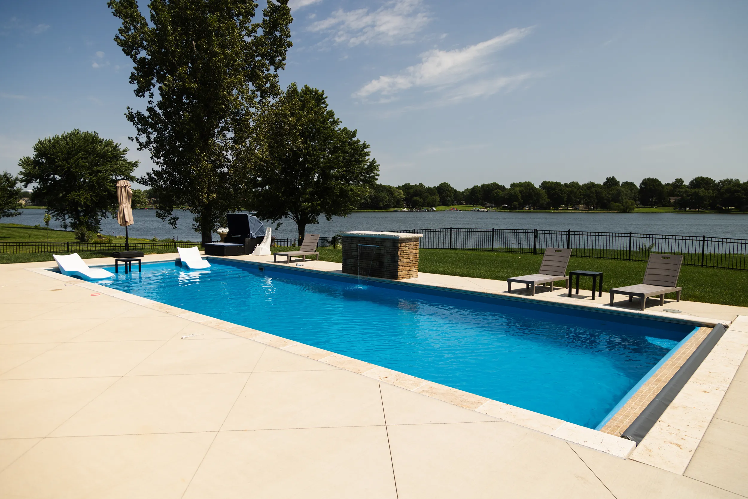Lakeside rectangular fiberglass pool with water feature and lounge chairs